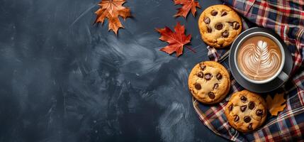 Autumn background with plaid, chocolate chip cookies and coffee cup with foam leaf on black table top view copy space banner autumn concept photo