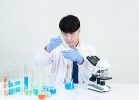 Portrait asian man student scientist wearing a doctor gown in the lab looking hand at chemist. caused by mixing reagents in scientific research laboratories with test tubes and microscope on the table photo