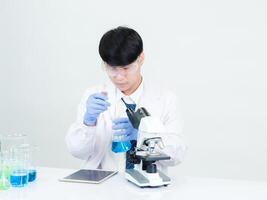 Portrait asian man student scientist wearing a doctor gown in the lab looking hand at chemist. caused by mixing reagents in scientific research laboratories with test tubes and microscope on the table photo