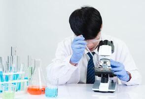 Portrait asian man student scientist wearing a doctor gown in the lab looking hand at chemist. caused by mixing reagents in scientific research laboratories with test tubes and microscope on the table photo