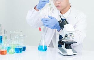 Portrait asian man student scientist wearing a doctor gown in the lab looking hand at chemist. caused by mixing reagents in scientific research laboratories with test tubes and microscope on the table photo