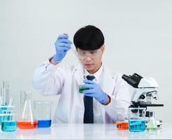 Portrait asian man student scientist wearing a doctor gown in the lab looking hand at chemist. caused by mixing reagents in scientific research laboratories with test tubes and microscope on the table photo