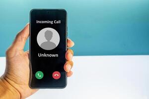 Hand holding a smartphone with incoming call from unknown number on the screen. Spammer incoming call concept. photo