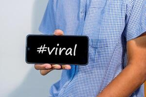 Man holding a smartphone with hashtag viral on screen. Viral content on social media concept. photo