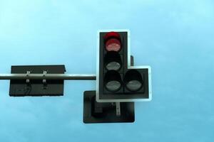 A traffic light hangs on a pole indicating a red signal to stop. On the back side are two signal indicators. under view of blue sky. photo