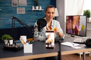 Blogger recording book review for her online talk skow. Creative vlogger making blog concept speaking and looking at smartphone on tripod home studio podcast using modern equipment. photo