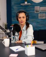 New media star looking at camera while talking into microphone during podcast. Social media influencer recording professional content with modern equipment and digital web internet streaming station photo