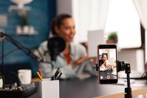 Influencer holding white gift box while recording videoblog for social media. Creative content creator making broadcast concept speaking and looking at smartphone on tripod at home studio podcast photo