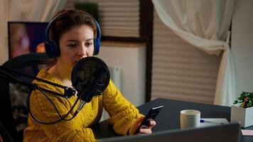 Internet show host answering at questions of fan texting on phone and talking at microphone from home podcast studio. Show production broadcast presenter streaming live content recording digital media photo