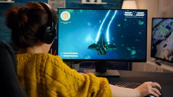 Pro gamer playing in the space shooter on personal computer. Woman gaming with teammates through headphones during online eSport tournament in action shot using technology network wireless photo