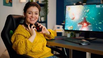 Woman gamer taking off headseat looking at camera smiling and playing in virtual shooter game championship in cyberspace, esports player performing on pc in stylish room during gaming tournament photo