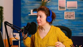 Podcaster recording online show at studio using headphones, microphone and laptop sitting in home podcast studio. On-air production internet broadcast show host streaming live content for social media photo