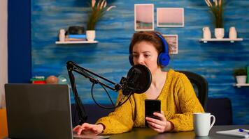 Blogger woman recording for her blog in home studio reading messages on smartphone. On-air online production internet broadcast show host streaming live content for social media photo