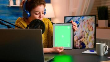 Influencer holding tablet with green screen and speaking into microphone during podcast in home studio. On-air production internet broadcast host streaming live content using chroma key mockup display photo