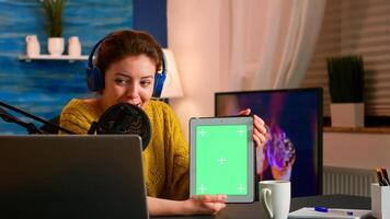 Influencer holding tablet with green screen display recording new podcast series for audience. Broadcast show host streaming live content for social media using mochup, chroma key, izolated desktop photo