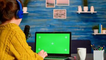 Vlogger reading at laptop with chroma key desktop during livestreaming from home studio. On-air production internet broadcast host streaming live content using mochup, green screen, izolated desktop photo
