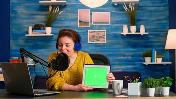 Vlogger looking at laptop and talking about tablet with chroma key desktop. On-air production internet broadcast host streaming live content using mochup, green screen, izolated desktop photo