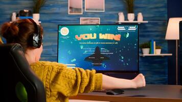 Back view of happy pro gamer winning space shooter game, raising hand celebrating, Virtual shooter game in cyberspace, esports player playing on computer game sitting at home, gaming tournament photo