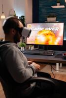 Professional player wearing vr goggles sitting on gaming chair playing online shooter game. Defeated man losing game tournament using joystick late at night in living room. photo
