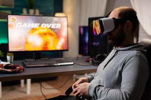 Defeated gamer man losing game tournament playing with virtual reality headset. Competitive player using joystick for online competition late at night in gaming room photo