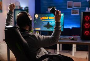 Winner gamer sitting on gaming chair at desk and playing space shooter games with controller. Man streaming online videogames for esport tournament in room with neon lights photo