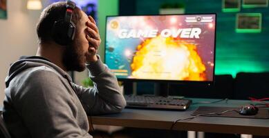 Gamer with headset and microphone losing games in gaming home studio and talking with friends on networks. Defeated man with headphones streaming online cyber performing during tournament photo
