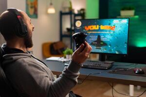 Videogame player raising hands after winning space shooter competition wearing headset. Professional pro gamer playing online videogames with new graphics on powerful computer from gaming room photo