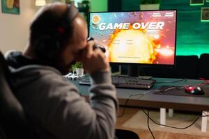 Competitive player losing e-sport championship using technology network wireless Defeated man playing online space shooter competition with powerful professional computer holding controller photo