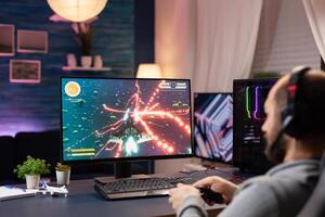 Man with headphones and joystick streaming space shoot videogames in gaming home studio. Professional player man talking with other players online for game competition playing at powerful computer photo