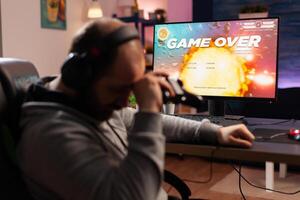 Addicted gamer losing space shooter videogame using headphones and wireless joystick. Upset player . Defeated gamer using professional equipment for online tournament late at night in gaming room photo