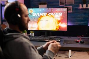 Disappointed esport gamer losing virtual tournament videogame using wireless controller. Defeated man playing online space shooter competition with powerful professional computer holding joystick photo