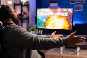 Game over for gamer playing videogames on computer during night time in gaming room home. Defeated man with headphones streaming online cyber performing through tournament photo