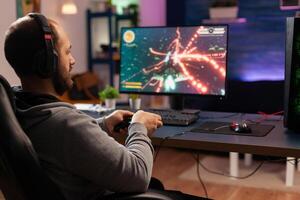 Concentrated gamer playing virtual game on powerful computer at home with professional headphones. Digital gamer using joystick for shooter space gaming competition late at night in living room photo