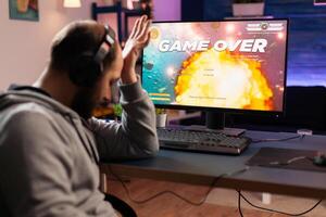 Portrait of sad upset gamer losing space shooter videogame. Defeated man with headphones streaming online cyber performing during gaming tournament using technology network wireless photo