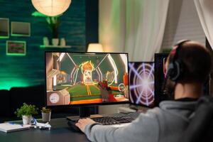 Back view shot of focused pro gamer streaming videogames on professional computer using headphones. Online streamer cyber performing during gaming tournament using technology network wireless photo