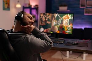 Competitive gamer streatching on gaming chair at desk and playing shooter videogames in studio home room. Online streaming cyber performing during game tournament using powerful PC with RGB photo