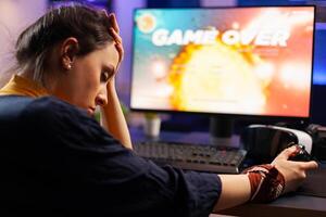 Pro videogames keeping his head on hand after losing space shooter game using wireless joystick . Defeated gamer wearing vr headphone for online championship sitting on gaming chair late at night photo