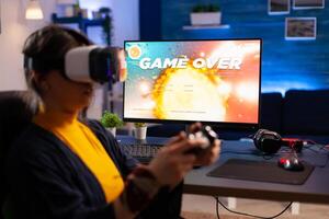 Game over for cyber gamer playing space shooter game using professional vr headphones. Defeated player using joystick for online championship sitting on gaming chair late at night in living room photo