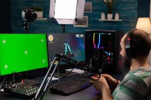 Professional cyber streamer playing digital videogames on professional powerful computer with green screen display. Player using pc with mock up chroma isolated desktop streaming shooter games photo