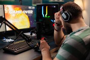 Videogame streamer losing videogame competition while wearing professional headset. Defeated gamer using modern controller for online tournament late at night in gaming room photo