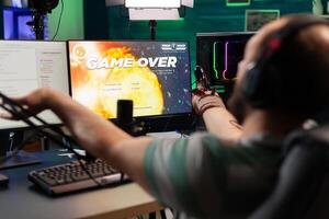 Game over for man streamer playing online space shooter game using modern headseat and joystick. Cyber performing on powerful pc talking with players on chat open during professional competition photo