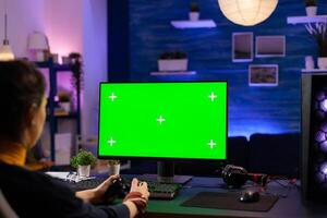 Competitive gamer looking into powerful pc with green screen display playing online games for live tournament. Cyber player using pc with mock up chroma isolated desktop streaming shooter games photo