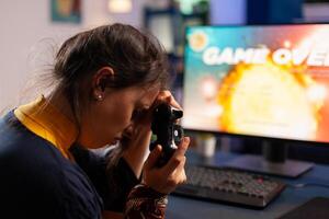 Professional gamer keeping her controller on hand after losing space shooter game using wireless joystick . Competitive player using modern equipment for online championship photo