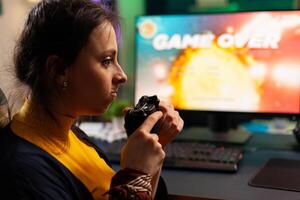 Pro player sitting on gaming chair at desk and losing space shooter games using console. Woman streaming online videogames for esport tournament in room with neon lights photo