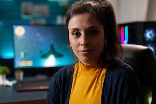 Portrait of woman gamer looking into camera after playing space shooter games using professional RGB keypad on powerful computer. Caucasian pro player streaming online videogames in home studio photo