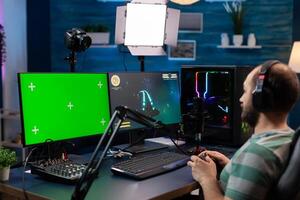 Caucasian man gamer streaming online videogames on professional powerful computer with green screen display. Streamer using pc with mock up chroma isolated desktop playing shooter games photo