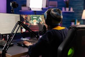 Professional streamer playing shooter games wearing headphones and talking into microphone via streaming chat. Gamer making online videogames with new graphics on powerful computer photo