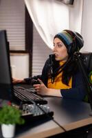 Side view of pro streamer with headphone playing shooter game competition using modern equipment. Player sitting on gaming chair using wireless console and talking with other gamers into microphone. photo