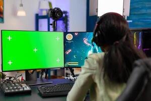 Back view of black gamer streams online game tournament on computer with green screen at night. Gamer using pc with greenscreen isolated desktop streaming space shooter games. photo