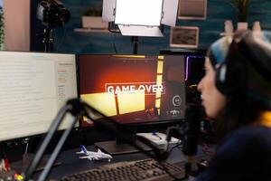 Game over for streamer talking into microphone with other players via streaming chat wearing headphones. Online cyber performer during gaming tournament using powerful PC with RGB photo